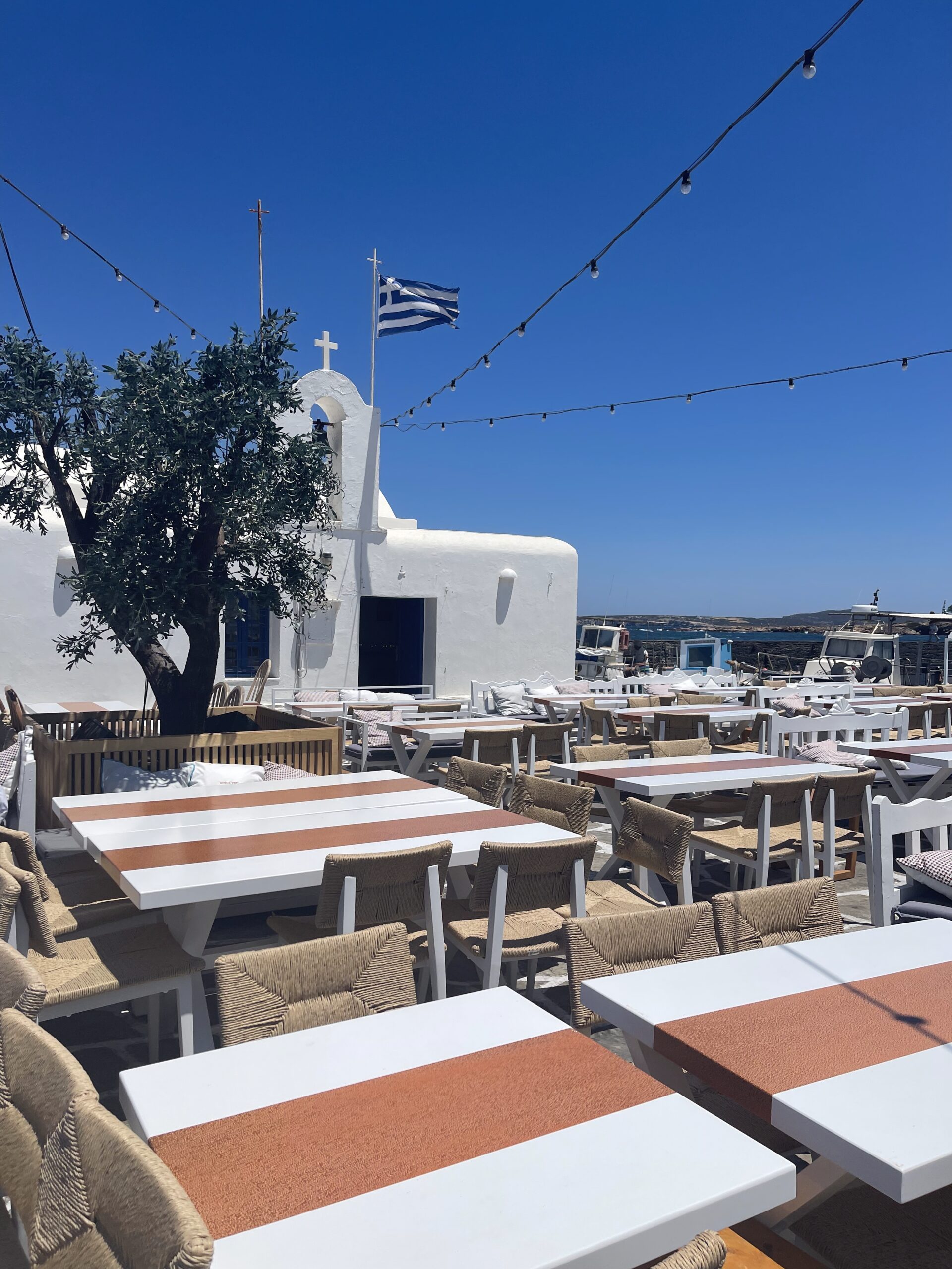 IMG_6043 Terrasse ensoleillée avec fanions et tables vides à Paros